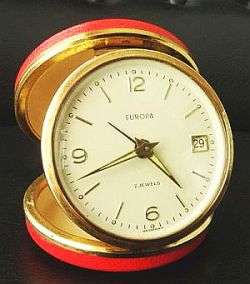 TRAVEL ALARM CLOCK WITH DATE BY "EUROPA" 2 JEWELS,ROUND IN RED ROUND CASE,WORKING,MADE IN GERMANY