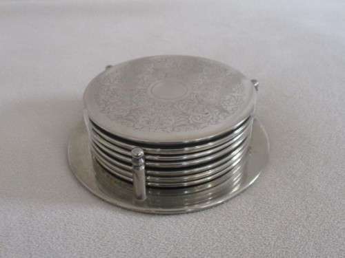 A SET OF SEVEN ETCHED SILVER METAL COASTERS WITH STAND