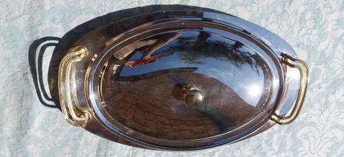 AN OVAL STAINLESS STEEL SERVING PLATTER WITH GOLD TONE HANDLES SOLD AS IS