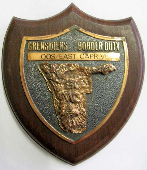 GRENSDIENS - BORDER DUTY : OOS/EAST CAPRIVI : WOODEN BASE - METAL BADGE :11.5cm WIDE - 13.5cm LONG