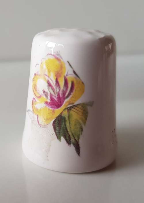 A Vintage collectors thimble. A white ceramic Thimble with painted flower in front.