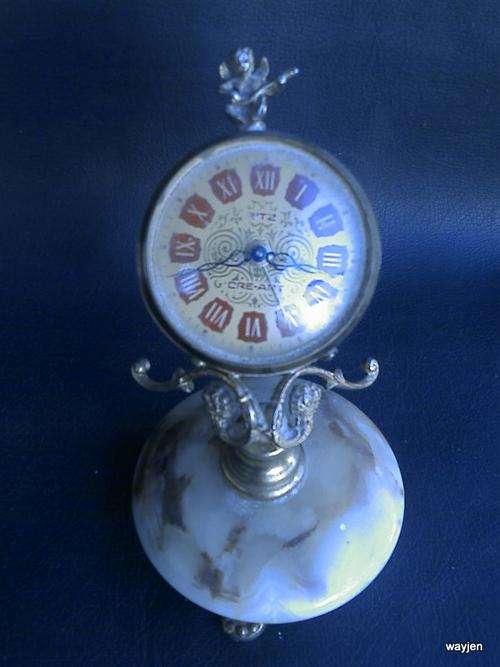 RITZ CRE-ART MANTEL CLOCK ON ONYX/MARBLE BASE. CLOCK COMES LOOSE FROM BASE. WORKING. CHERUB ON TOP.