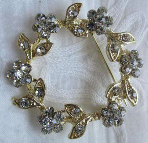 DAINTY AND SPARKLING BROOCH, GOLD TONE SET WITH A CIRCLE OF FLOWERS AND LEAVES OF GLASS CRYSTALS.