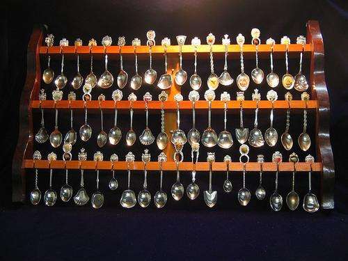 Collection of 54 souvenir spoons on wooden display rack