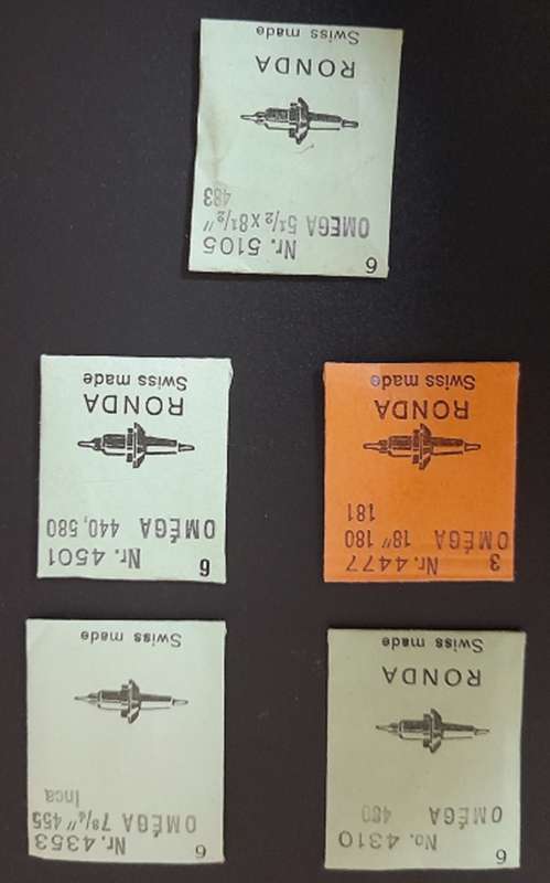 Omega wrist watch parts. New balanced staffs in sealed package envelopes