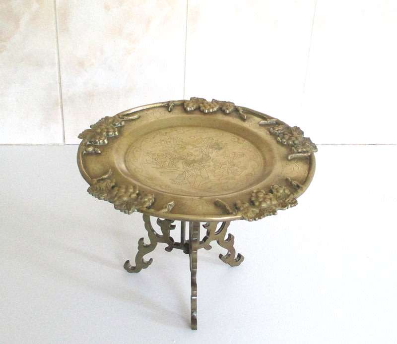 A VINTAGE BRASS PLATE EMBOSSED WITH FRUIT AND ETCHED CENTER ON A STAND