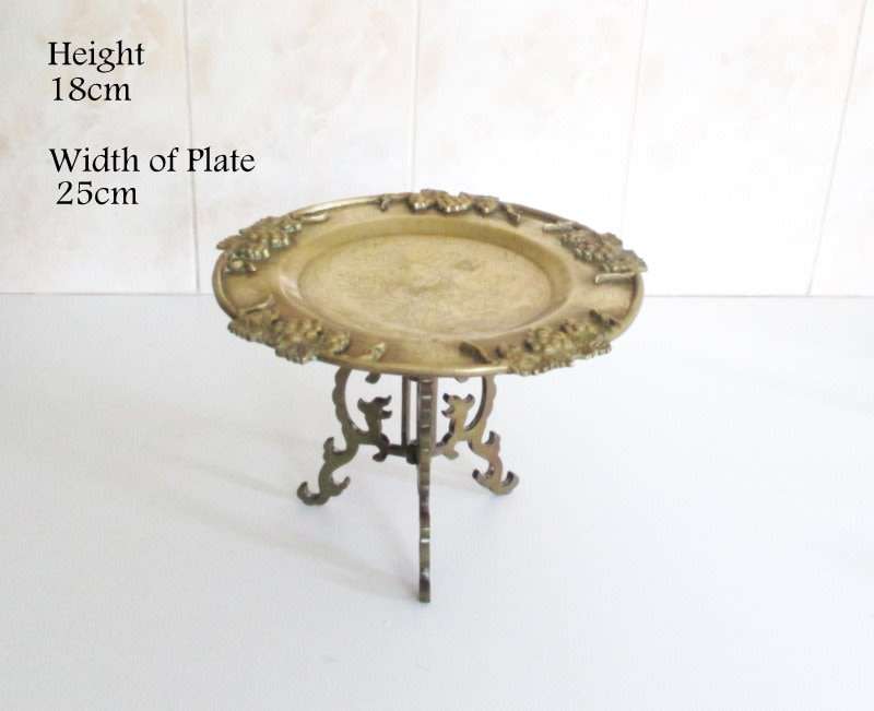 A VINTAGE BRASS PLATE EMBOSSED WITH FRUIT AND ETCHED CENTER ON A STAND