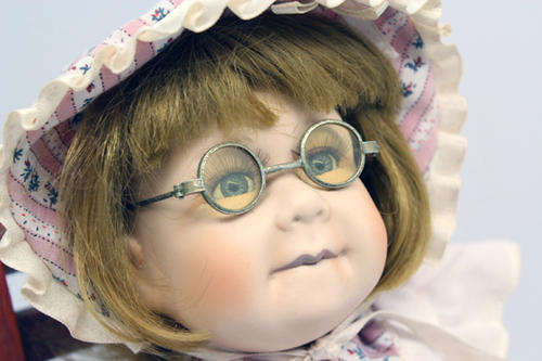 Little Porcelain Doll Girl Wearing Spectacles In Wooden Chair