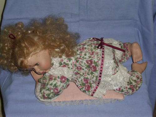 A BEAUTIFUL PORCELAIN DOLL BLUE EYED-DRESSED-LYING DOWN ON CUSHION-45CM IN LENGTH-20CM IN HEIGHT