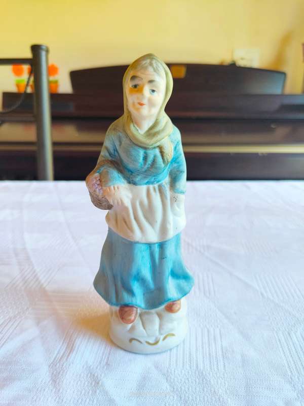 A vintage figurine of an old lady carrying grapes in a basket