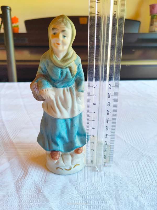A vintage figurine of an old lady carrying grapes in a basket