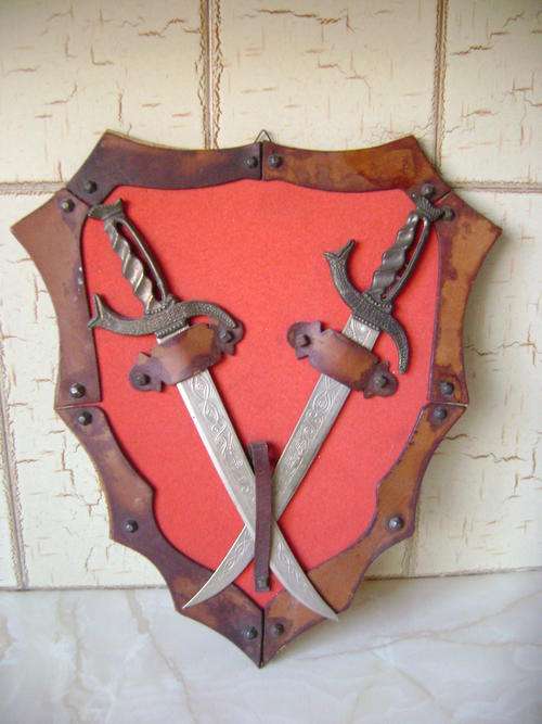 OLD SHIELD WITH KNIVES DISPLAYED ON IT
