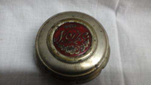 LOVELY PLATED ROUND TRINKET JAR WITH LID WITH NOZZE WRITTEN ON A RED BACK GROUND.