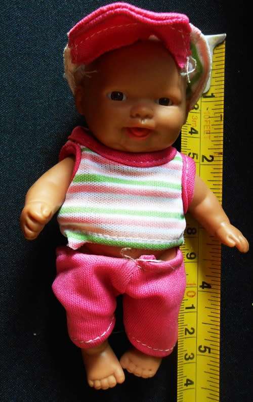 Small light  brown Baby doll in a bright pink utfit with cap. Looks like a Berenguer doll