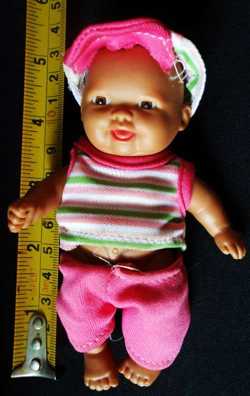 Small light  brown Baby doll in a bright pink utfit with cap. Looks like a Berenguer doll