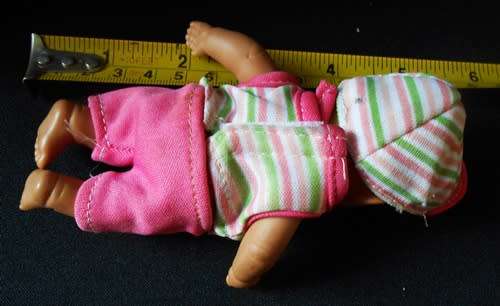 Small light  brown Baby doll in a bright pink utfit with cap. Looks like a Berenguer doll