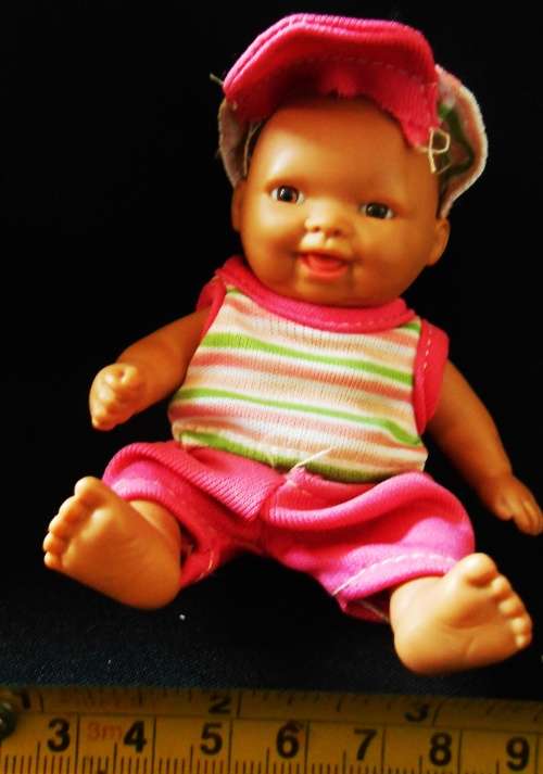 Small light  brown Baby doll in a bright pink utfit with cap. Looks like a Berenguer doll