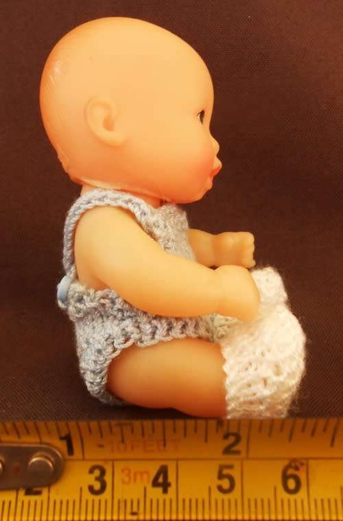 collectable small baby doll in sitting position in hand knitted outfit