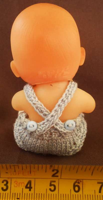 collectable small baby doll in sitting position in hand knitted outfit