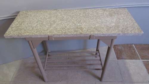 A VERY HANDY TO HAVE A METAL STAND WITH A GRANITE TOP PERFECT FOR CUTTING AND SERVING BY THE BRAAI