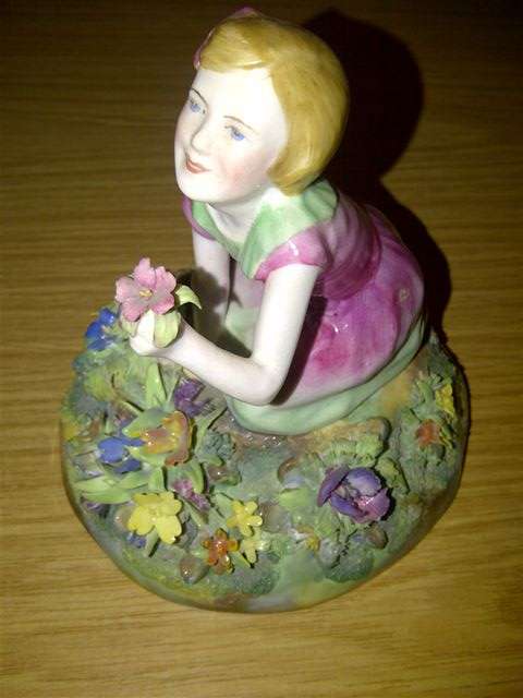 FIGURINE, of a Young Girl kneeling amongst flowers and holding out a single blossom, 14cm high,