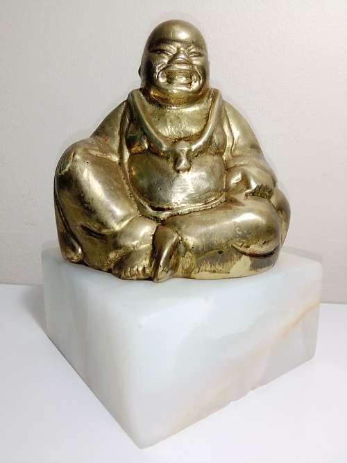 A laughing solid Brass Buddha on white Marble plinth. Symbol of prosperity in Feng Shui.
