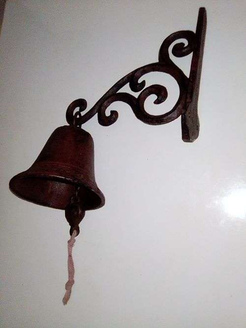 A Old school front door Cast Iron Bell hanging on a nice scrolled bracket.