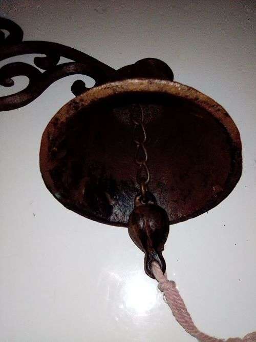 A Old school front door Cast Iron Bell hanging on a nice scrolled bracket.