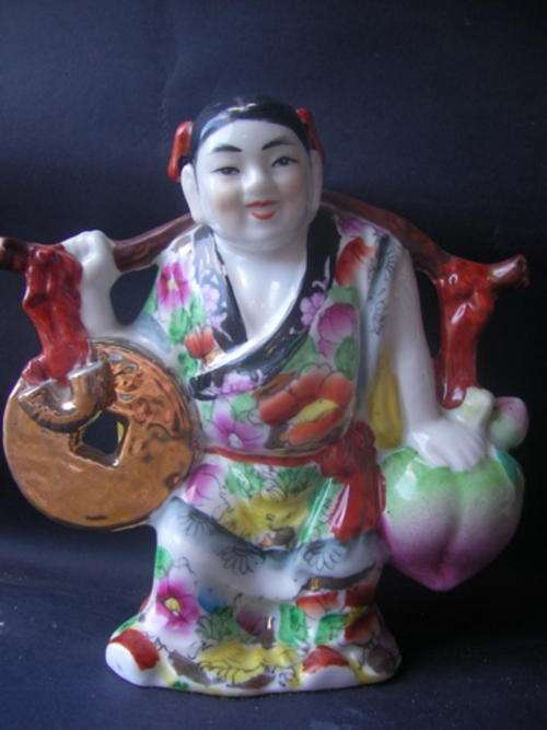 JOLLY AND HAPPY CHINESE FIGURE IN IMARI STYLE. CARRYING WHAT APPEARS TO BE A GIANT VEGETABLE (TURNIP
