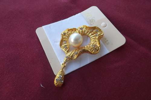 Unique gold toned brooch with faux pearl in middle,small shiny stones and hanging teardrop.
