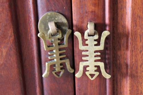 A beautifully carved oriental Elm wood "end" cupboard with brass symbol handles and a drawer