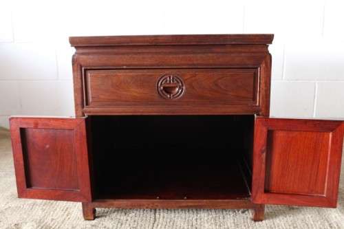 A beautifully carved oriental Elm wood "end" cupboard with brass symbol handles and a drawer