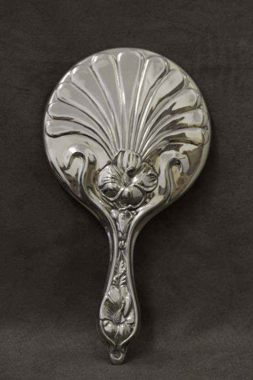 A beautiful, vintage ladies round chrome hand held vanity mirror with flower detailing on the back.