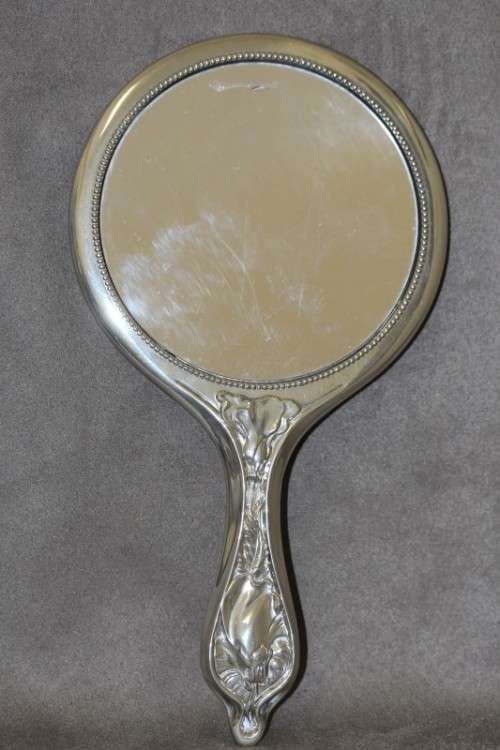 A beautiful, vintage ladies round chrome hand held vanity mirror with flower detailing on the back.