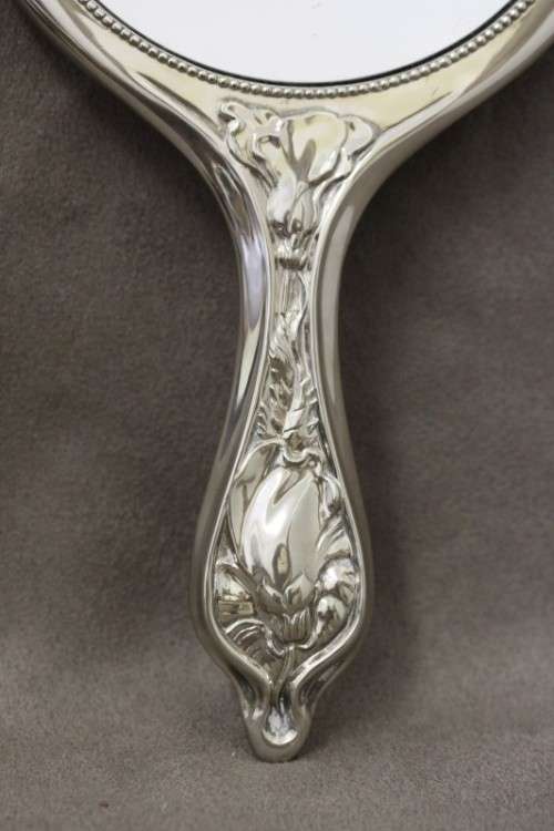 A beautiful, vintage ladies round chrome hand held vanity mirror with flower detailing on the back.