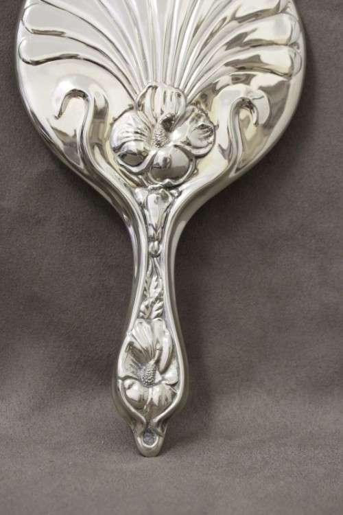 A beautiful, vintage ladies round chrome hand held vanity mirror with flower detailing on the back.