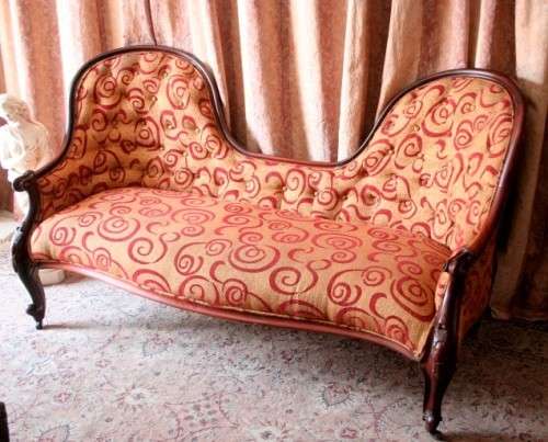 An antique Victorian  "parlour settee" couch w carved detailing and period upholstery on castors.