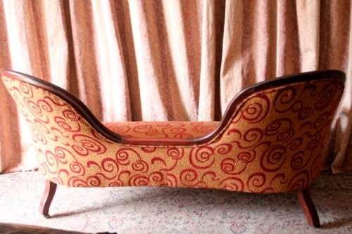 An antique Victorian  "parlour settee" couch w carved detailing and period upholstery on castors.