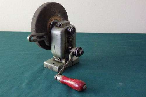 AN AWESOME VINTAGE HAND CRANKED GRINDING WHEEL WITH A TABLE MOUNTABLE METAL CASING AND WOODEN HANDLE