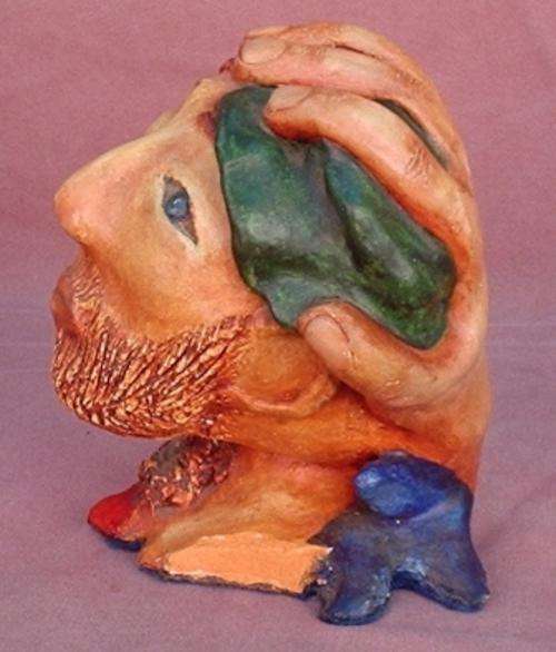 Ugly old clay head - half female face, half male - with a protective hand over the back of the head