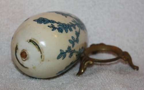 LARGE DECORATIVE CERAMIC EGG . WHITE BACKGROUND WITH BLUE RIBBON AND FLORAL DETAIL ON A LOOSE METAL