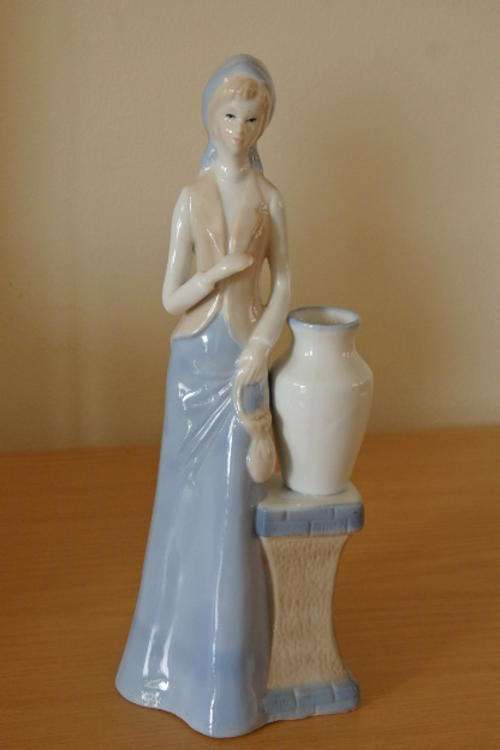 A GORGEOUS TALL PORCELAIN FIGURINE OF A YOUNG LADY NEXT TO A LARGE WATER VASE