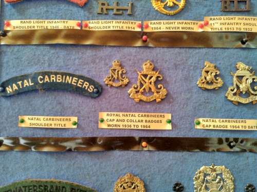Display of South African Traditional Regiments cap/beret badges, shoulder titles and collar badges.