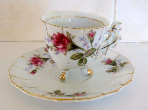 A SMALL CUP AND SAUCER ON THREE FEET