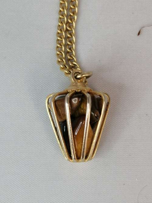 AN UNUSUAL CAGED TIGERS EYE PENDANT ON A GOLD TONE CHAIN