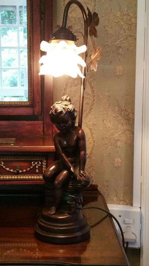 A Pseudo Bronze Lamp , cast as a seated child beneath a realistic pink rose shade