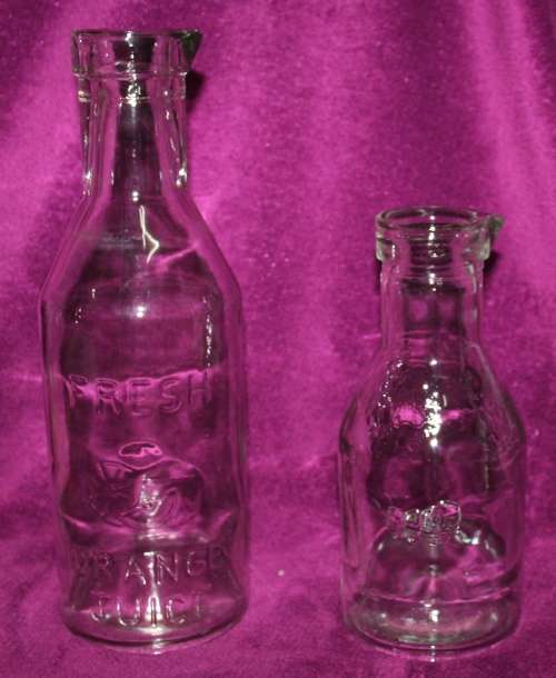 TWO STUNNING GLASS JUISE/MILK DECANTER BOTELS ONE EMBOSSED WITH FRESH ORANGE JUICE ON THE SIDE