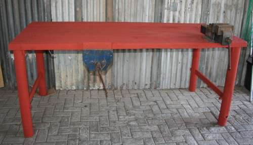 A VERY LARGE WORK BENCH WITH A HEAVY METAL FRAME AND THICK WOODEN TOP WITH A VICE FITTED ON TOP