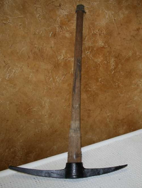 This is a vintage farming pickaxe. It  features a wooden handle and metal spear