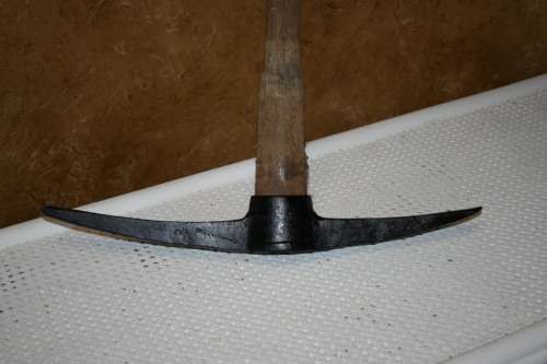 This is a vintage farming pickaxe. It  features a wooden handle and metal spear